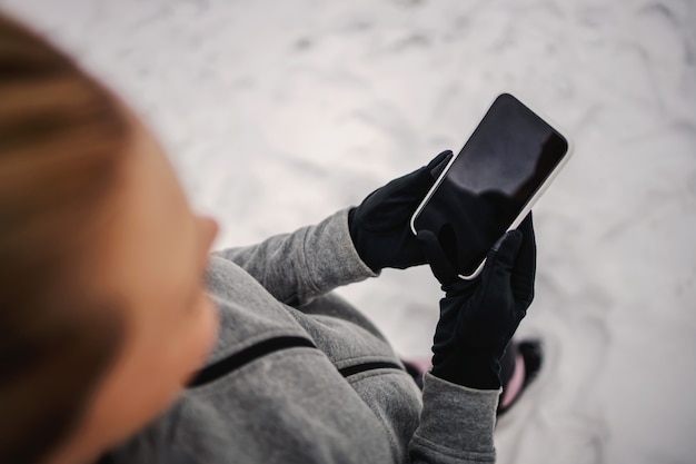 Mains tenant un téléphone intelligent. Gros plan d'une femme tenant un téléphone en se tenant debout dans la nature sur la neige. Télécommunications, technologie, médias sociaux