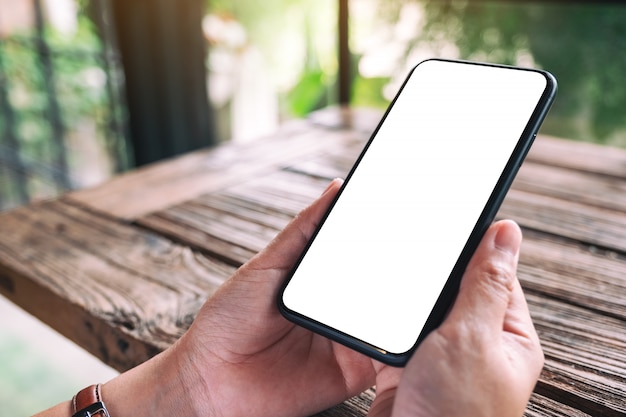 mains tenant un téléphone mobile noir avec écran de bureau vide sur table en bois