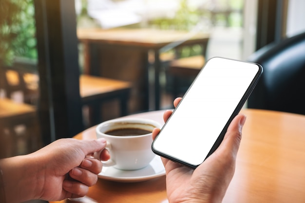 mains tenant un téléphone mobile noir avec écran de bureau vide tout en buvant du café