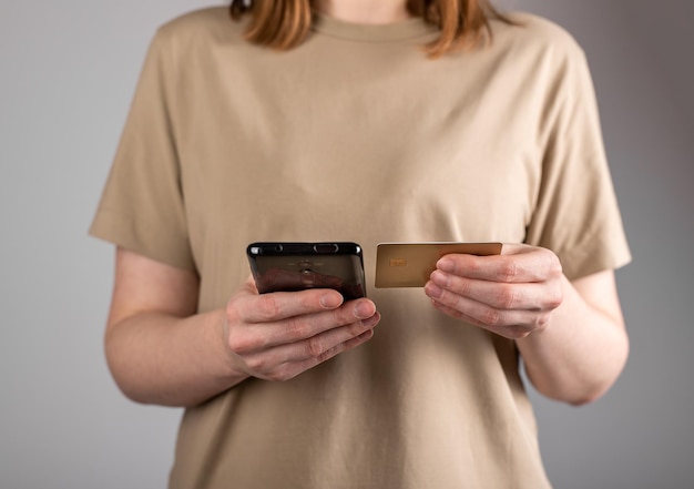 Mains tenant un téléphone portable et une carte de débit à l'aide d'une application bancaire pour payer les achats en ligne sur Internet