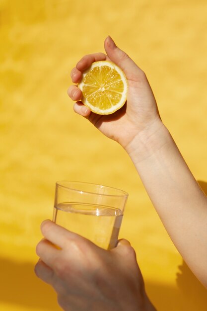 Photo mains tenant une tranche de citron et un verre d'eau