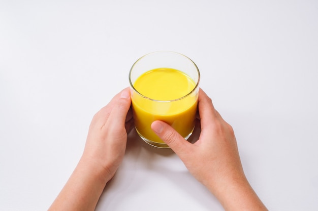 Mains tenant un verre de latte au curcuma au lait doré sur fond de tableau blanc