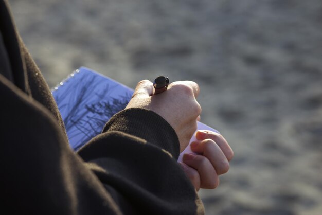 mains tendues d'une fille en sweat à capuche noir dessinant avec un crayon gris dans un carnet de croquis