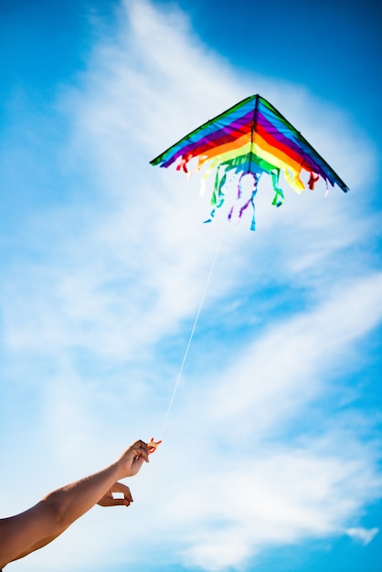 Les mains tiennent un beau et lumineux cerf-volant arc-en-ciel