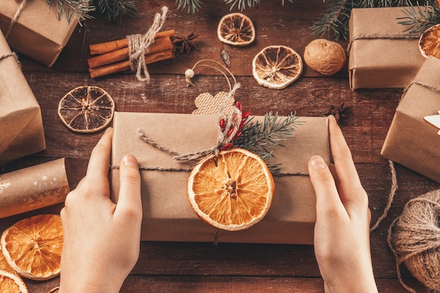 Les Mains Tiennent Un Cadeau De Noël Emballé Dans Du Papier Kraft Et Des Matériaux Naturels. Concept De Nouvel An Vert