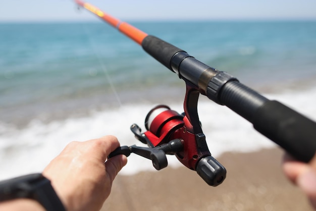 Les mains tiennent une canne à pêche dans le contexte de la côte de la mer