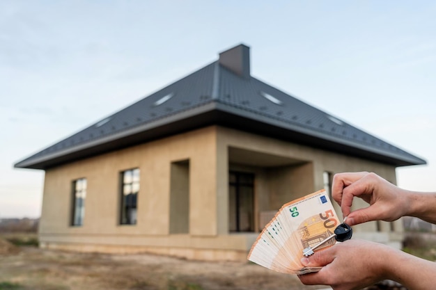 Les mains tiennent des clés et de l'argent devant la maison Projet de construction passant à un nouveau loyer hypothécaire et achetant un bien immobilier