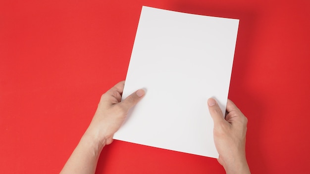 Les mains tiennent le papier A4 blanc sur fond rouge.