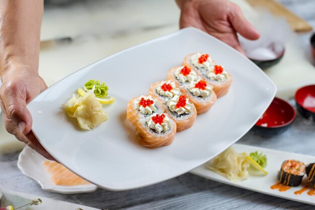 Les mains tiennent la plaque avec des sushis. Sushi au citron et au wasabi. Caviar de saumon sur rouleaux d'uramaki. Repas japonais aux épices.