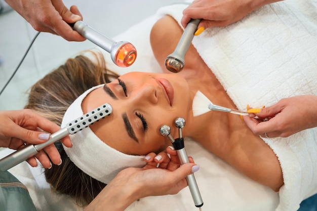 Photo les mains tiennent un tas d'outils de cosmétique le visage de la femme se fait soigner par les mains d'une esthéticienne au salon de spa