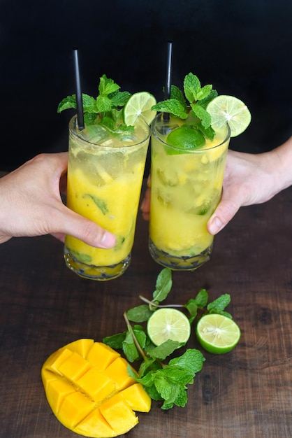 Mains tinter les verres avec du mojito à la mangue sur fond noir avec des tranches de mangue et de citron vert