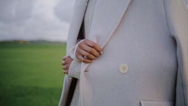 Des mains touchant un manteau d'automne par temps froid, un gros plan d'une femme élégante ajustant ses vêtements.