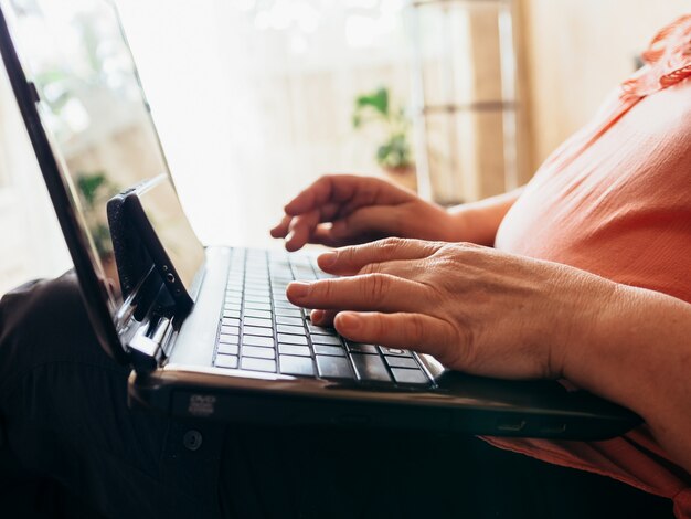 Mains d'une vieille femme sur un clavier d'ordinateur portable.