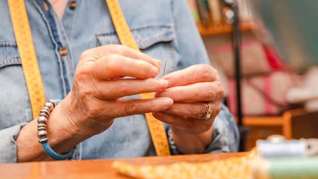 Mains d'une vieille femme enfilant une aiguille à coudre