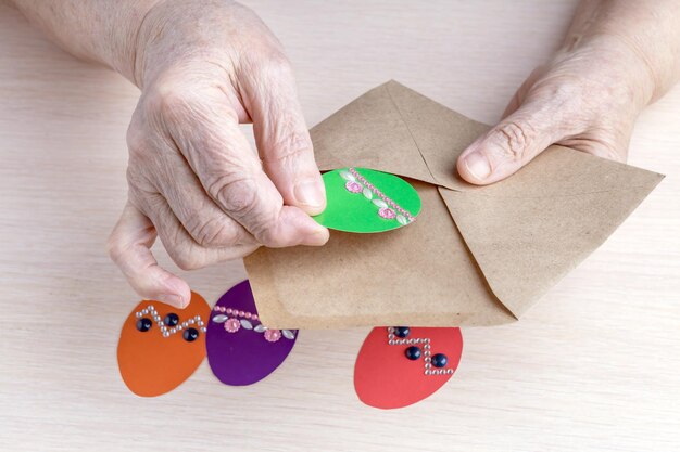 Les mains d'une vieille femme mettent des oeufs de Pâques en papier dans une enveloppe