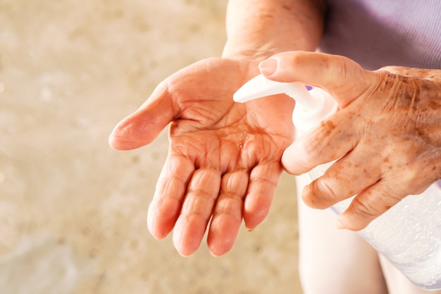 Mains de vieille femme en poussant le distributeur de pompe de désinfectant