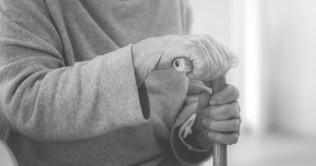 Les mains d'une vieille femme tenant une canne dans la pièce noire et blanche