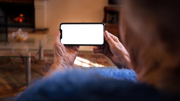 Les mains d'une vieille femme tiennent un smartphone avec un écran blanc vide pour votre maquette