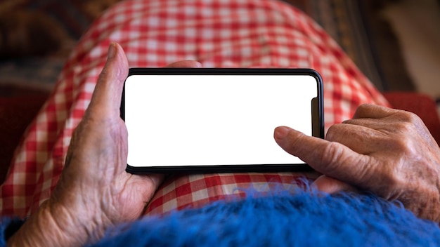 Les mains d'une vieille femme tiennent un smartphone avec un écran blanc vide pour votre maquette