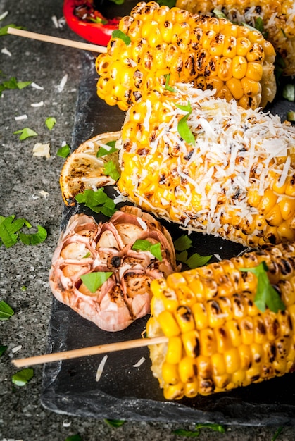 Maïs grillé avec une pincée de fromage, piment fort et citron sur une table en pierre sombre.