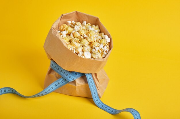 Maïs soufflé dans un sac en papier avec ruban à mesurer bleu sur fond jaune