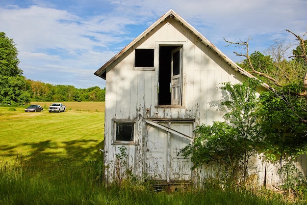 Une maison abandonnée et en décomposition à la campagne avec des portes cassées et des fenêtres envahis par la végétation.