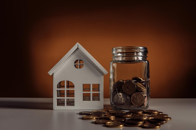 Maison blanche et bocal en verre avec des pièces de monnaie sur un concept de prêt et d'hypothèque de table