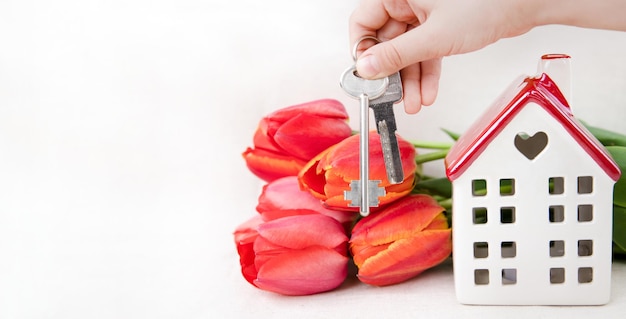 Une maison blanche avec des clés d'appartement au toit rouge et des tulipes sur fond blanc