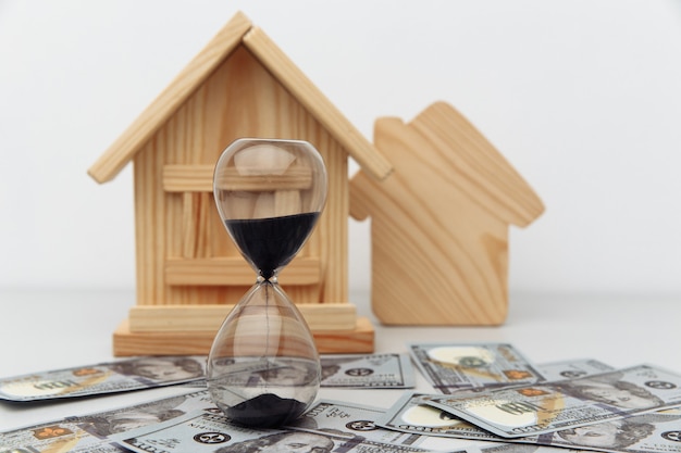 Maison en bois et horloge sur les billets en dollars l'achat ou la vente de concept immobilier