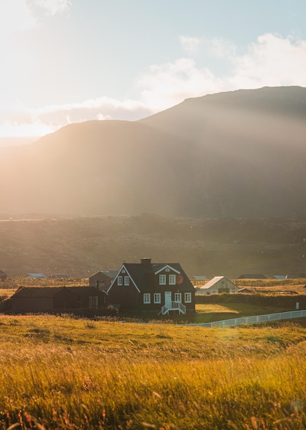 Maison en bois islandais brillant de lumière du soleil sur le pré et oiseau volant au coucher du soleil l'été au village de pêcheurs d'Arnarstapi Islande