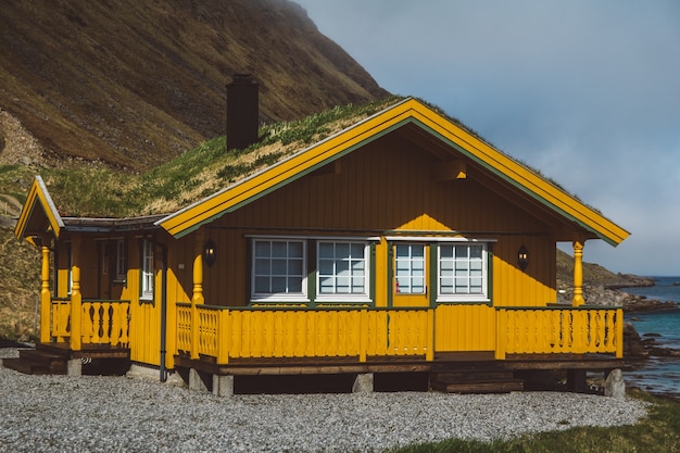 Maison en bois jaune avec de la mousse sur le toit sur fond de mer et de montagnes.