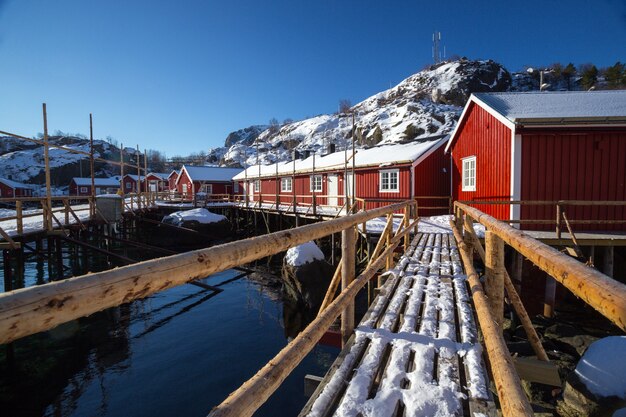 Maison En Bois Norvégienne Traditionnelle Rorbu Pour Se Tenir Sur Le Rivage Du Fjord Et Des Montagnes Au Loin. Iles Lofoten. Norvège.