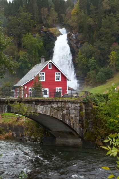 Maison en bois traditionnelle norvégienne et vieux pont en arc avec cascade au loin