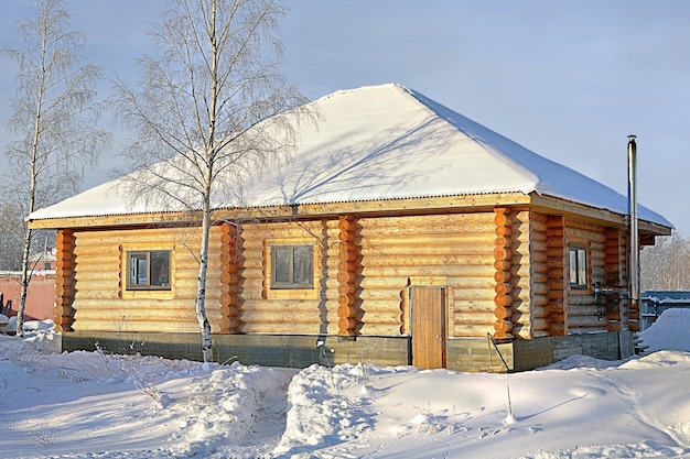 Maison de campagne en bois de bois teinté jaune, hiver neigeux, journée ensoleillée.