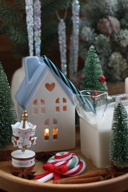 Une maison du Nouvel An avec une bougie allumée à l'intérieur des décorations de Noël sur un plateau en bois avec des bougies allumées et un verre de lait