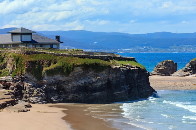 Maison sur falaise et plage de sable de l'Atlantique d'été Los Castros (Galice, Espagne).