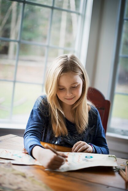 Une maison familiale Une jeune fille assise à une table dessinant sur une grande feuille de papier Tenant un crayon