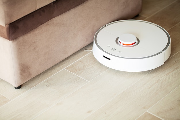 Maison intelligente. Le robot aspirateur tourne sur un plancher de bois dans un salon.