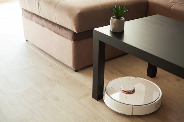 Maison intelligente. Le robot aspirateur tourne sur un plancher de bois dans un salon.