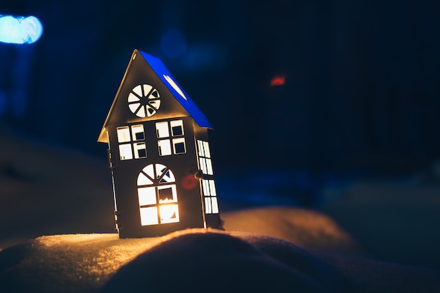 Photo maison lanterne avec bougie allumée sur la neige le soir.