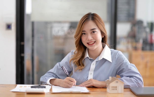 Maison miniature entre les mains d'une femme asiatique agent immobilier prêt à domicile travaillant au bureau en regardant la caméra