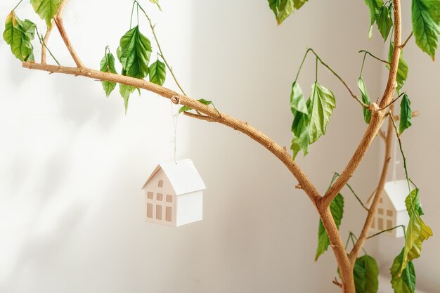 Maison miniature en papier blanc accrochée à une branche d'arbre