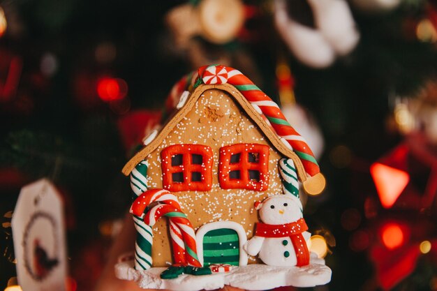 Maison de Noël faite de biscuits en pain d'épice décorée dans un esprit de Noël avec un sapin de Noël en arrière-plan