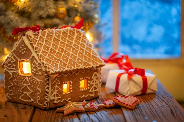 Maison de pain d'épice et cadeaux sous le sapin de Noël avec lumière