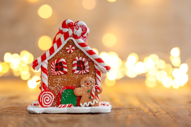 Maison en pain d'épice sous un arbre de Noël avec des lumières défocalisés.