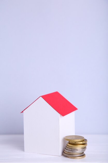 Maison en papier blanc avec toit rouge, avec des pièces sur fond gris