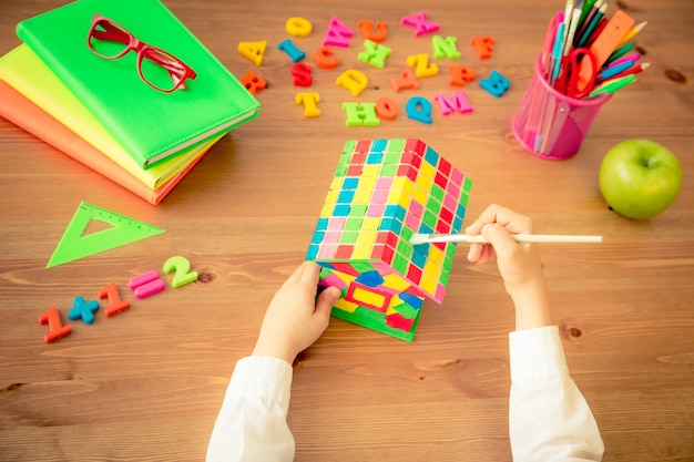 Maison de peinture d'enfant. Articles scolaires sur un bureau en bois en classe. Notion d'éducation. Vue de dessus