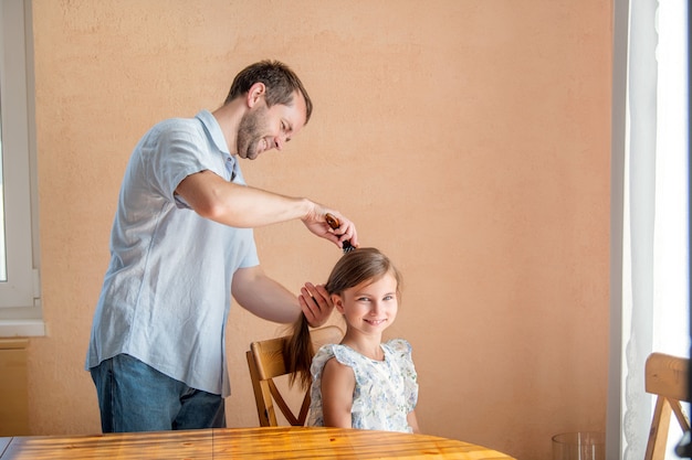 A la maison, le père brosse les cheveux de sa fille.