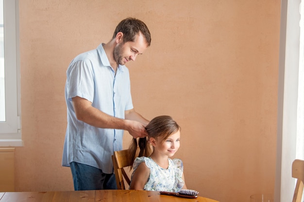 A la maison, le père brosse les cheveux de sa fille.