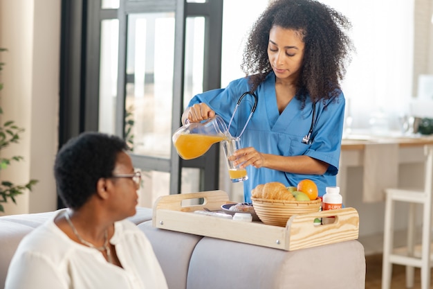 En maison de retraite. Infirmière versant du jus d'orange et apportant le petit-déjeuner à une dame vivant dans une maison de retraite